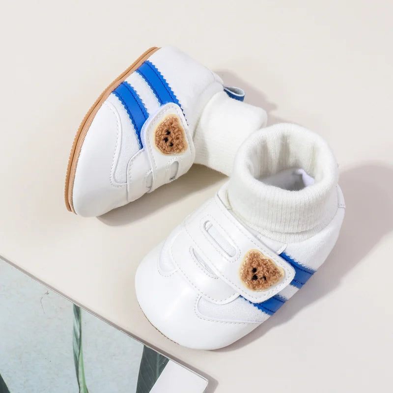 White baby booties with blue stripes and tan faux fur accents shown from the side.