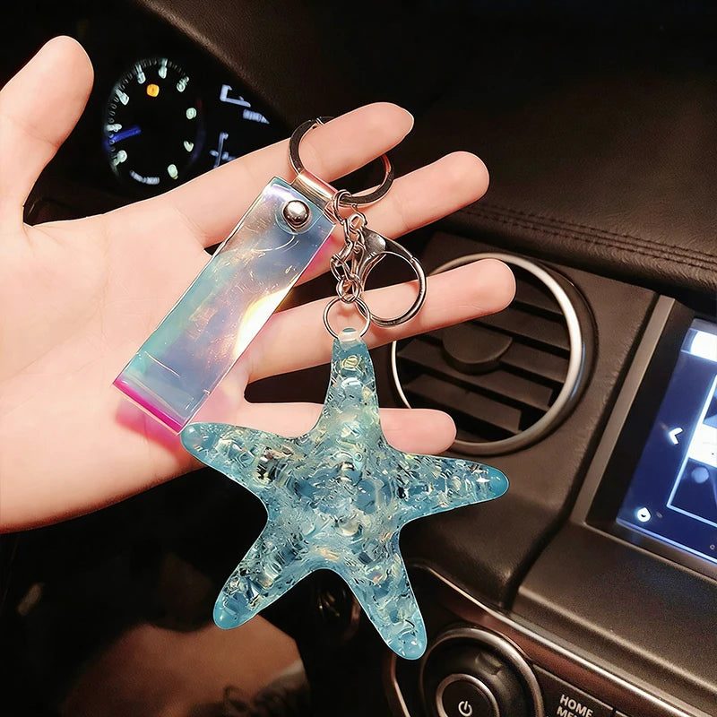 A hand holds a clear blue starfish beaded keychain charm against a dark car interior background.