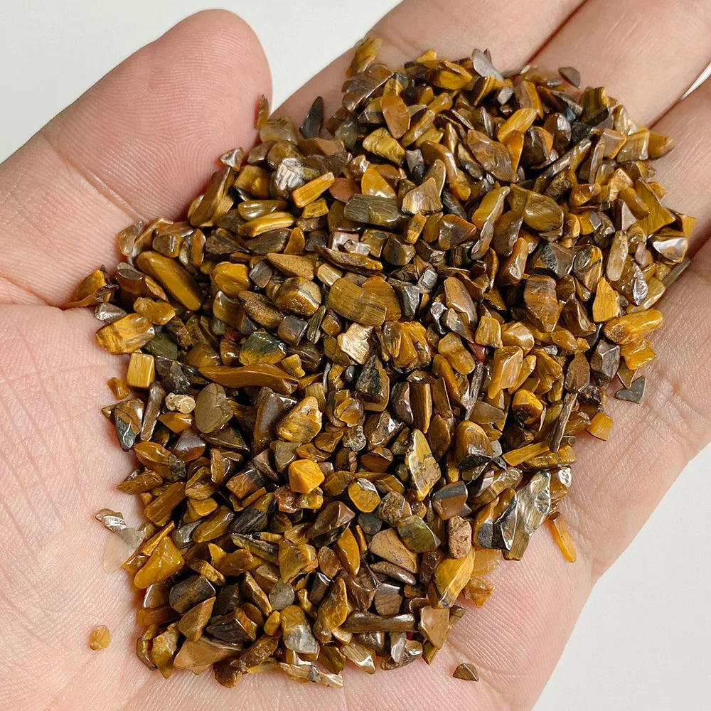 A hand holds a pile of natural tumbled stone chips in various shades of brown and gold.