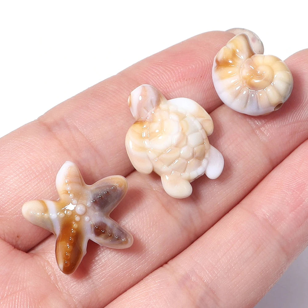 A variety pack of acrylic beads shaped like a starfish, conch, and turtle on a hand.