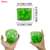 A hand holds a clear plastic jar of green jelly putty slime kit containing fruit pieces like leaves, watermelon, and grape sc