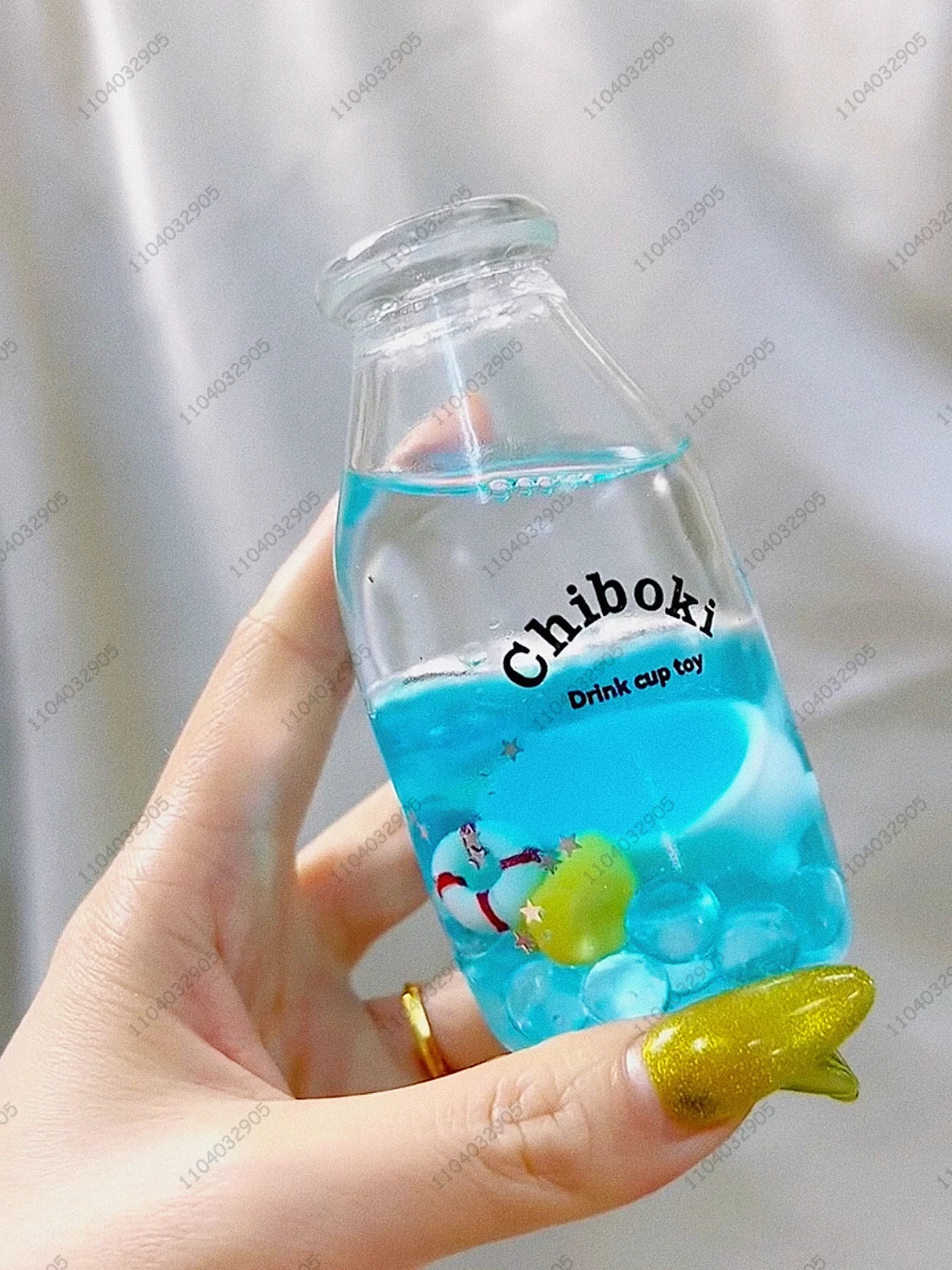 A hand holds a clear bottle filled with blue liquid labeled Chiboki drink cup toy