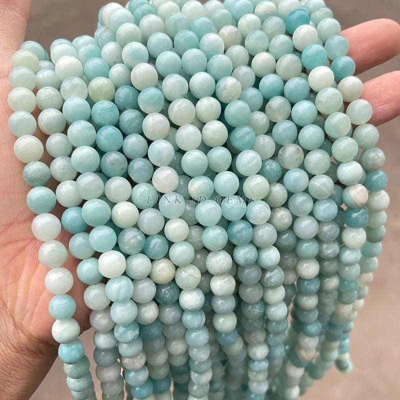 A hand holds a strand of light blue and white natural amazonite beads for jewelry making