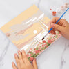 Hands paint a watercolor abstract sunset landscape on a canvas, surrounded by paint and brushes.