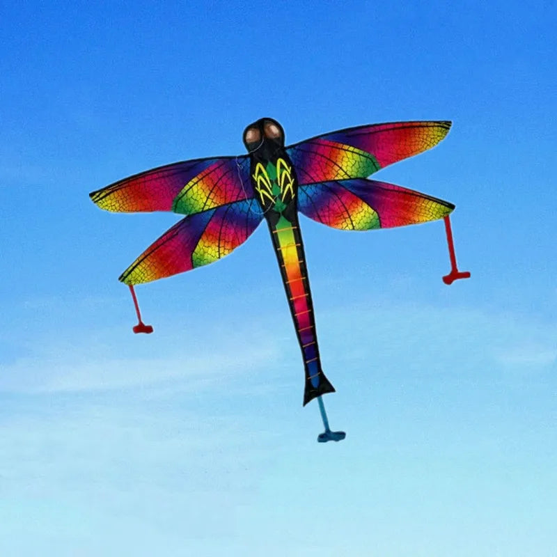 A colorful rainbow nylon kite with a black body and wings is flying against a clear blue sky.