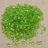 A pile of bright green tulip flower glass beads scattered on a beige fabric surface.