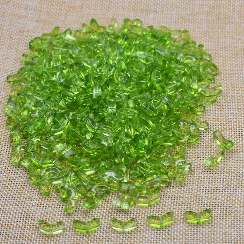 A pile of bright green tulip flower glass beads scattered on a beige fabric surface.