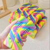 A hand holds several colorful butter stick squishies with yellow, pink, and green gradients.