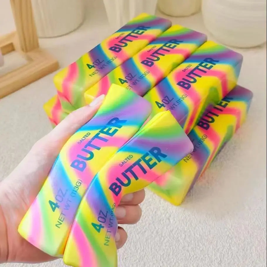 A hand holds several colorful butter stick squishies with yellow, pink, and green gradients.