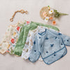 A collection of cute waterproof baby bibs with long sleeves in various patterns and colors laid out on a light fabric.