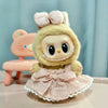 A cute plush doll wearing a pink ruffled dress and bow, with light blonde hair.