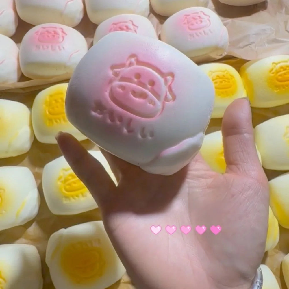 A hand holds a pink squishy milk bread stress relief toy surrounded by other yellow and white squishies.
