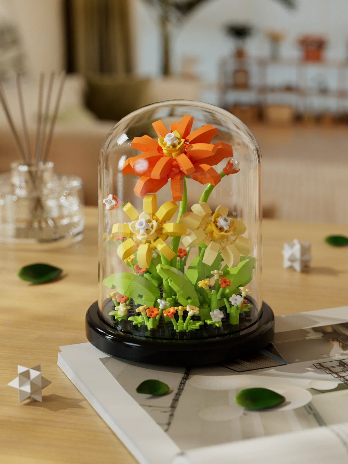 A glass display featuring an orange and yellow buildable eternal rose flower kit with green foliage.
