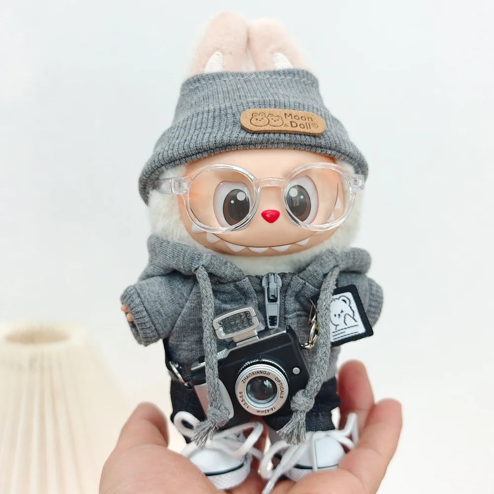 A Labubu doll wearing a gray hoodie and headphones, held in a person's hand.