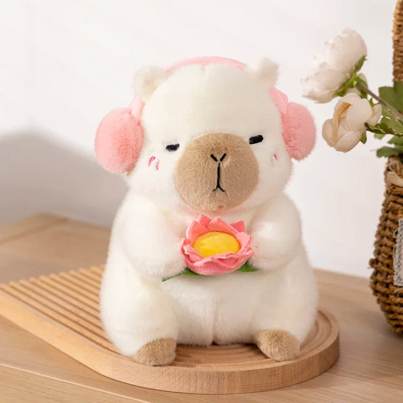 A white capybara plush toy is sitting and gently holding a pink lotus flower.