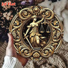Gold wall art sign featuring a female figure holding scales surrounded by ornate foliage and vines.