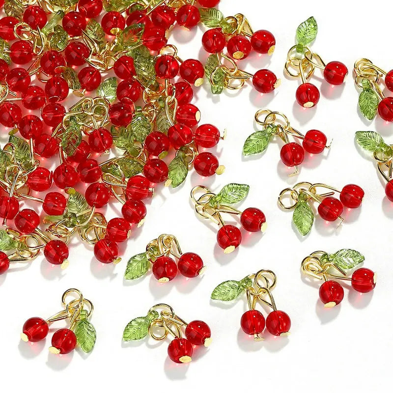 A collection of red cherry glass charms with gold-toned wire stems and green leaves for jewelry making.