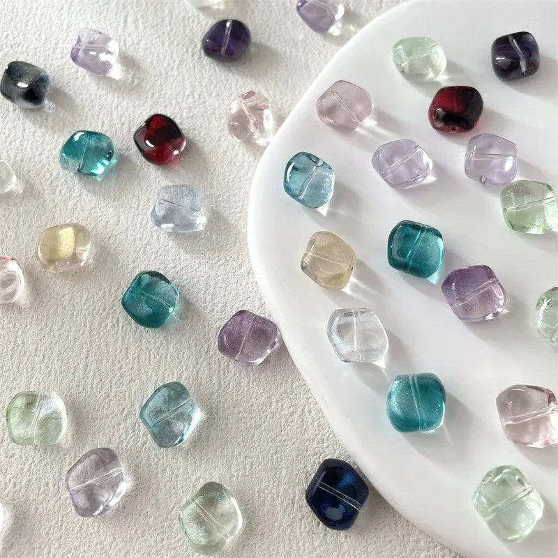 A collection of irregular square geometric glass beads in various shades of purple, blue, and green on a white surface.