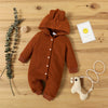 A brown knitted hooded baby romper lying on a wooden surface with a small yellow tag and a white animal toy.