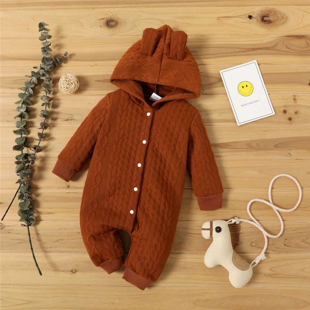 A brown knitted hooded baby romper lying on a wooden surface with a small yellow tag and a white animal toy.