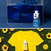 A yellow t-shirt with a bottle of Rit blue fabric dye placed on green moss with sunflowers.