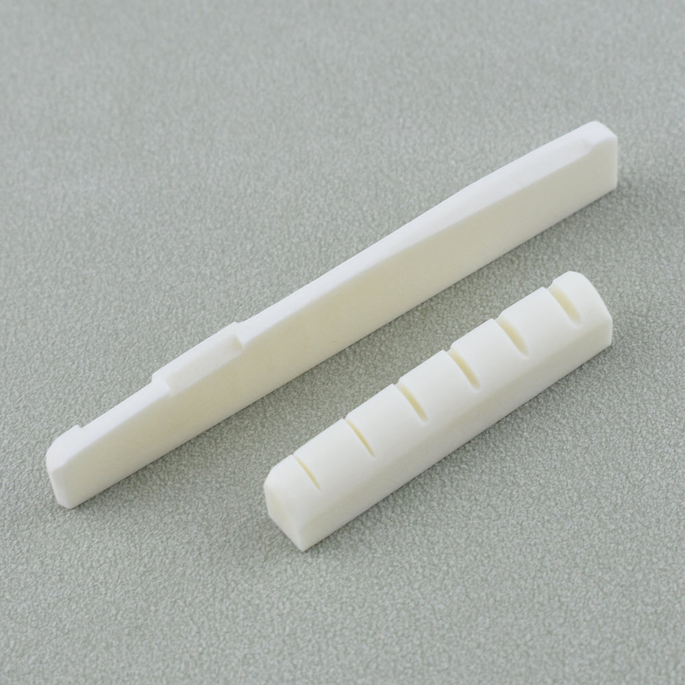 A white real bone guitar nut and bridge saddle shown diagonally on a gray surface.