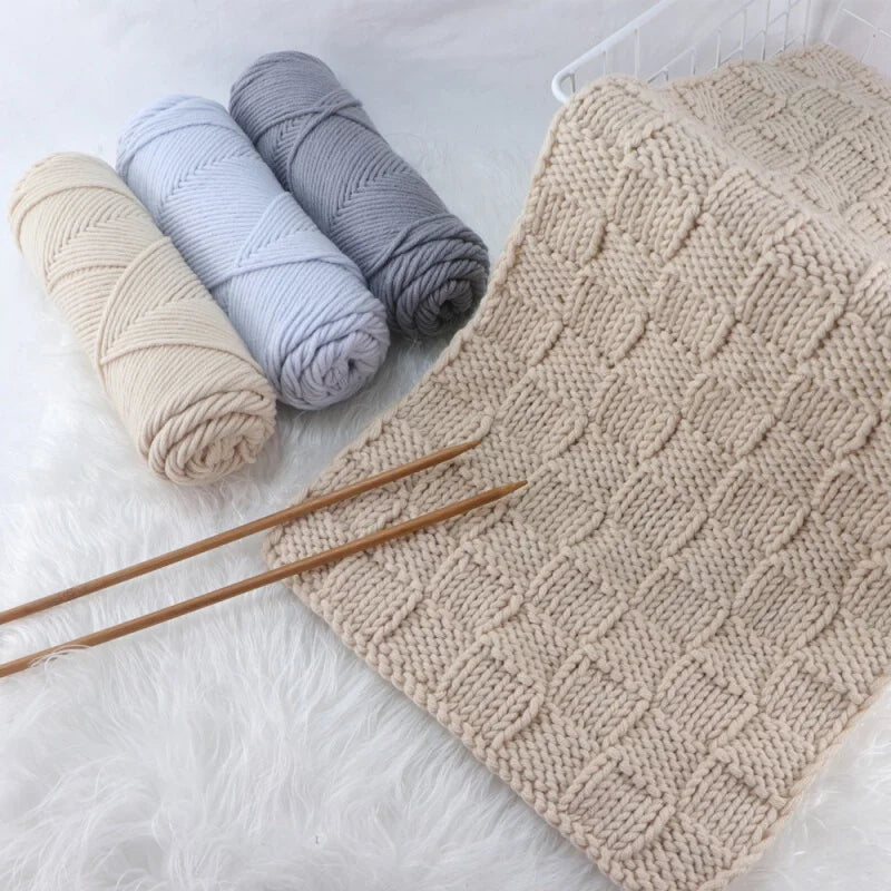 Three skeins of soft cotton blend yarn in beige, light blue, and gray next to a knitted swatch.