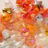 A collection of colorful acrylic bow and flower beads in shades of orange, pink, and clear are displayed for DIY jewelry maki