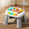A white musical baby piano playmat with a light-up keyboard and hanging toys sits on a wooden floor.