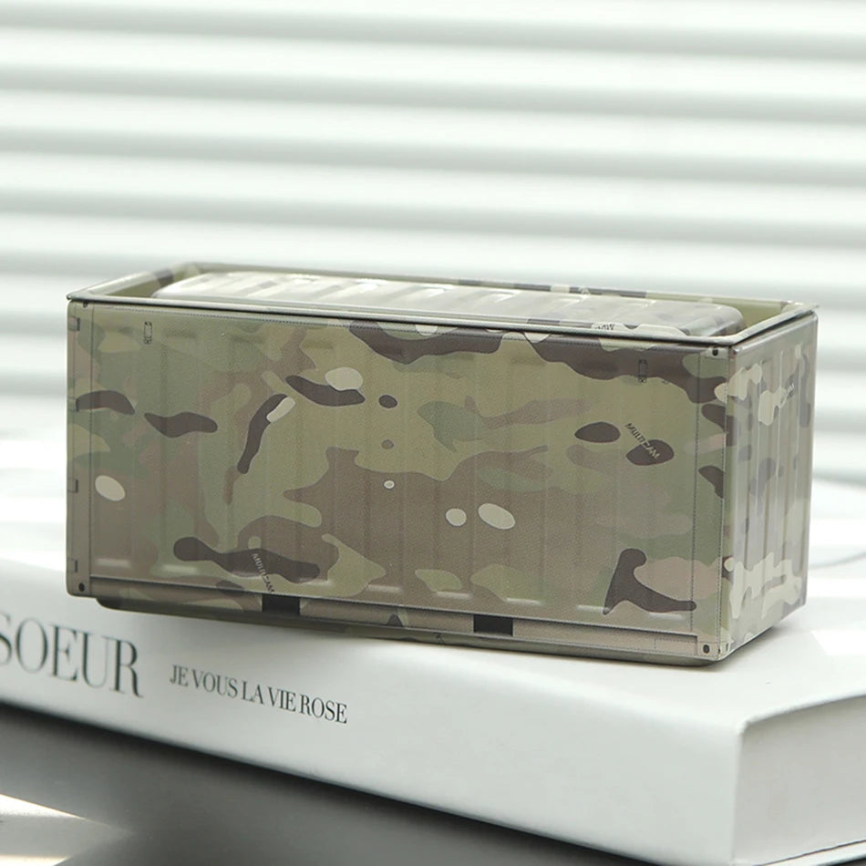 A miniature industrial iron storage box featuring a camouflage pattern resting on a white book.