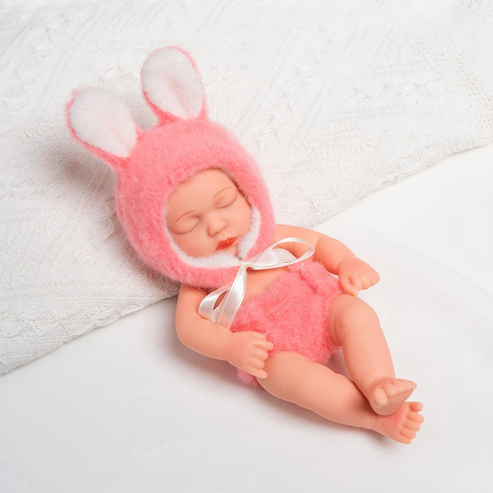 A realistic soft vinyl baby doll with pink ears and a matching outfit lying on a white towel.