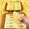 A hand is holding a block of yellow butter, surrounded by many other blocks in a woven basket.