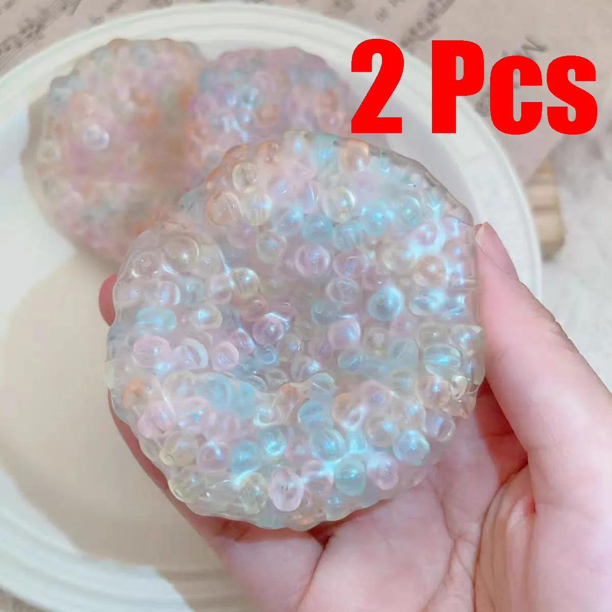 Two clear, iridescent squishy stress relief balls are held in a hand against a white background.