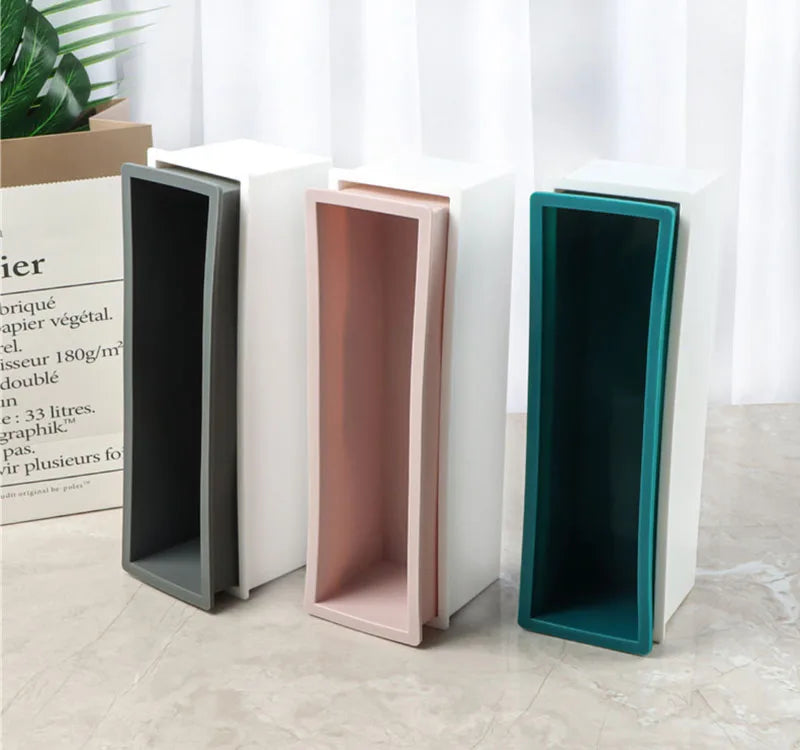 A set of silicone rectangle soap molds in various colors, including gray, pink, and teal, displayed next to a wooden box.