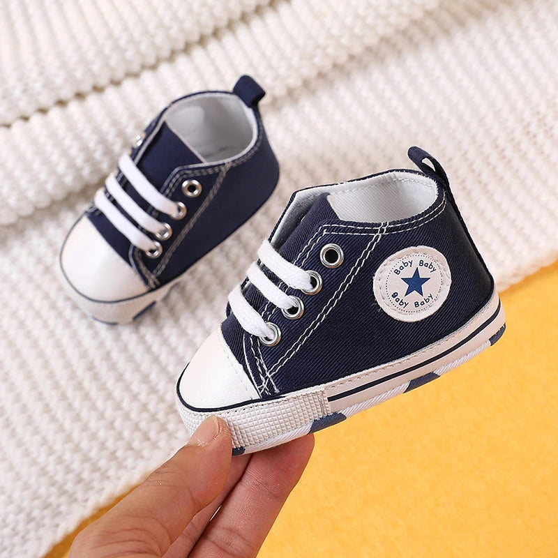 A pair of navy blue and white canvas baby shoes for infants resting on a yellow surface.