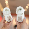 A pair of white soft sole sandals shaped like bears for a baby's first steps being held in hands.