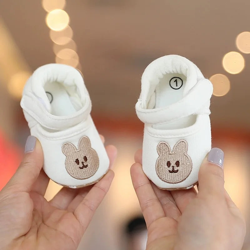 A pair of white soft sole sandals shaped like bears for a baby's first steps being held in hands.