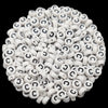 A close-up view of numerous white acrylic alphabet letter beads scattered on a dark background.