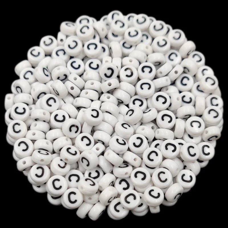A close-up view of numerous white acrylic alphabet letter beads scattered on a dark background.