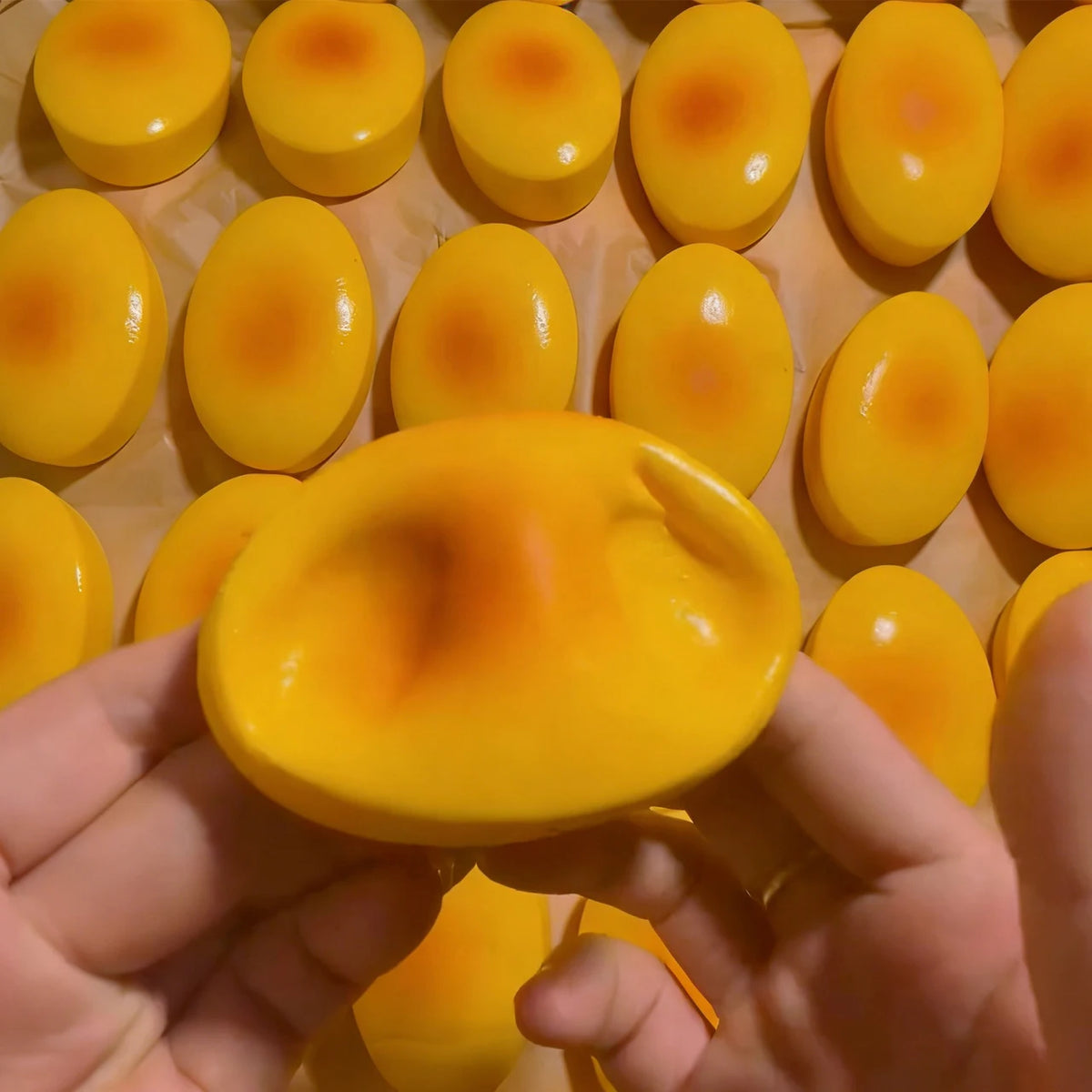 A hand holds a yellow cheese-shaped squishy stress relief toy with orange accents.