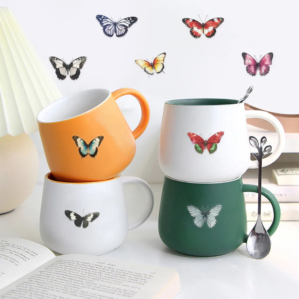 A collection of watercolor butterfly stickers is displayed on mugs and a white surface.
