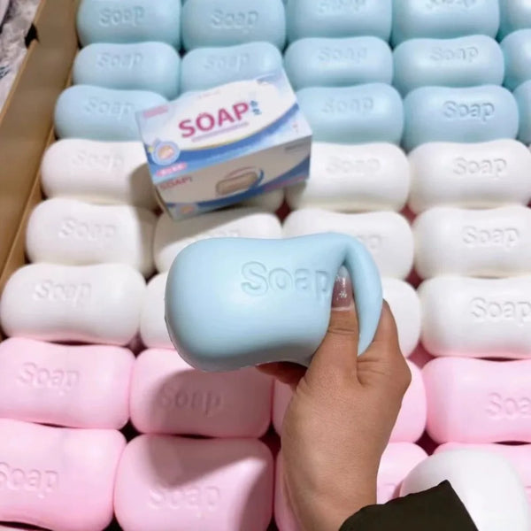 A hand is holding a light blue stress relief squishy soap toy among many white and pink soaps.