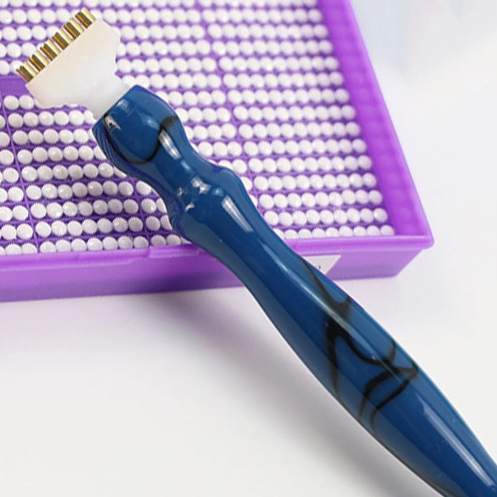 A blue diamond painting pen with an interchangeable tip rests in a purple box lined with white beads.