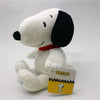 A white Snoopy plush toy with black ears and a red collar sitting on a clear stand.