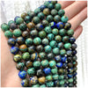 A hand holds a strand of natural stone beads featuring various shades of green, blue, and brown stones.