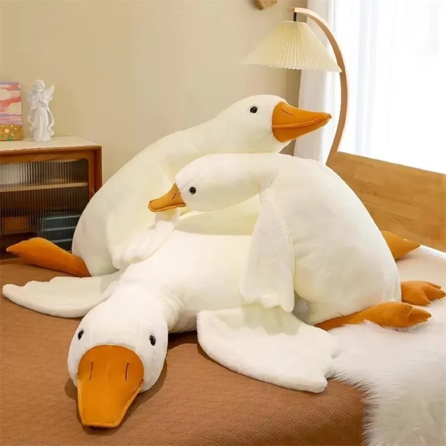 A white goose plush toy lying on a brown surface next to a wooden shelf.