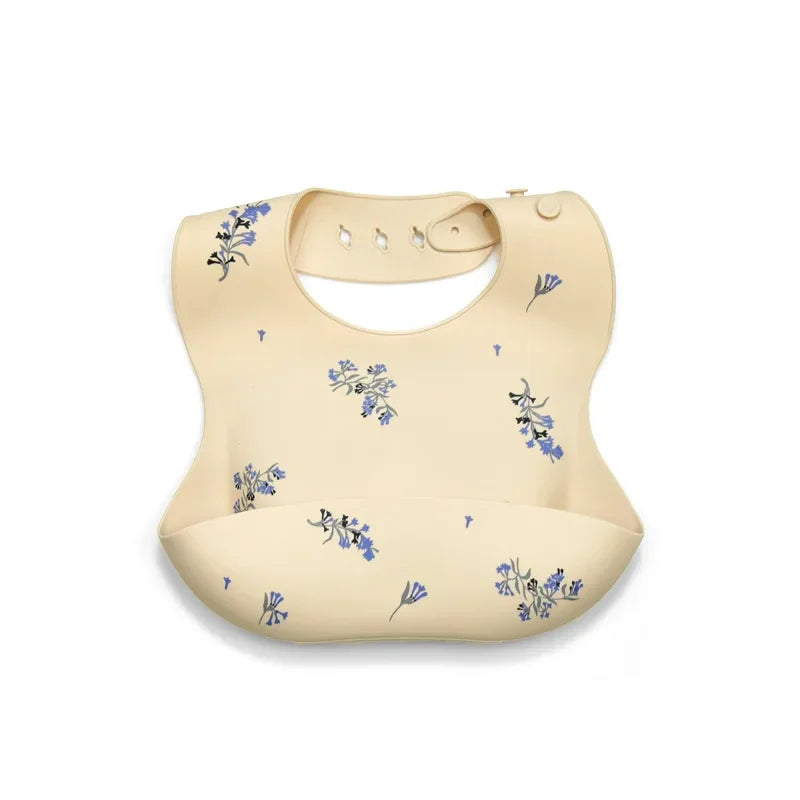 A beige soft silicone waterproof baby bib with an adjustable neck, featuring small blue floral patterns.