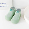A pair of light green knitted soft sole socks for babies and toddlers displayed on a white surface.