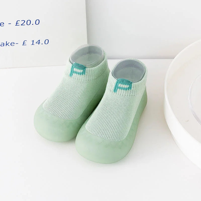 A pair of light green knitted soft sole socks for babies and toddlers displayed on a white surface.