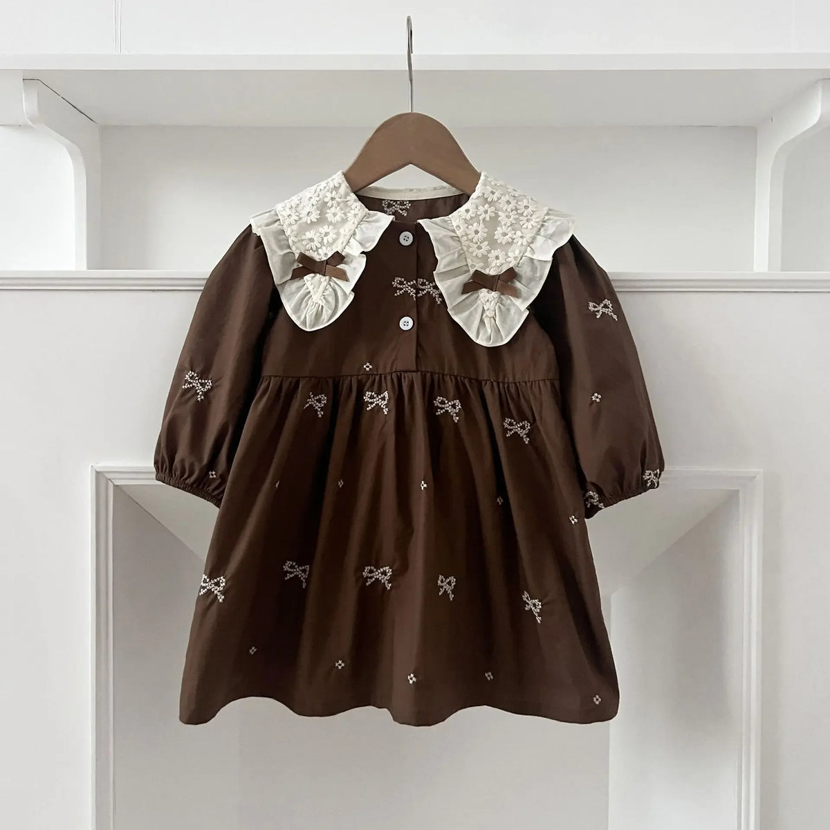 A brown cotton party dress for girls featuring white lace collar and embroidered details, displayed on a hanger.
